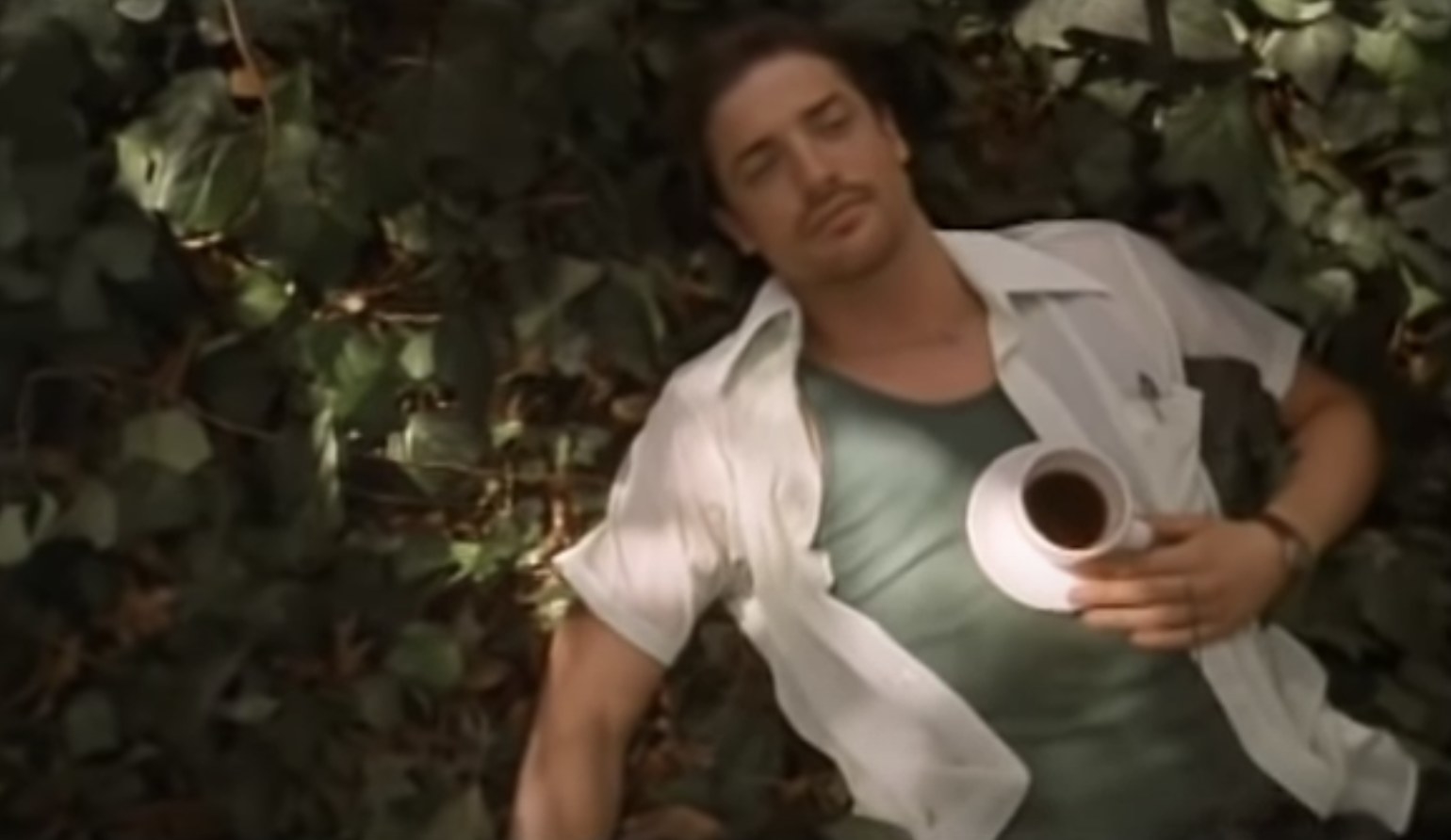 Brendan Fraser lies on a pile of leaves with a cup of coffee balanced on his chest.