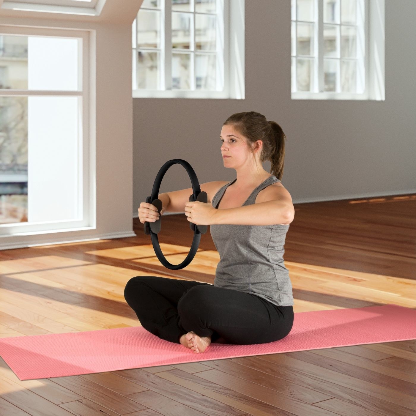 A woman sits crosslegged on a yoga mat and holds a Pilates ring