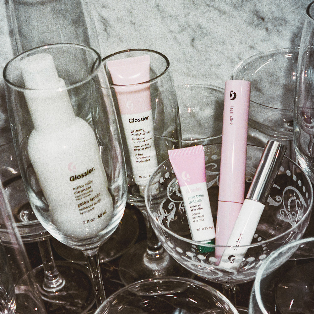 a bunch of Glossier products in pretty drinking glasses