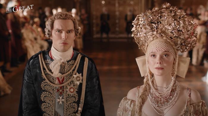 The couple played by Nicholas Hoult and Elle Fanning standing side-by-side as they wear royal regalia