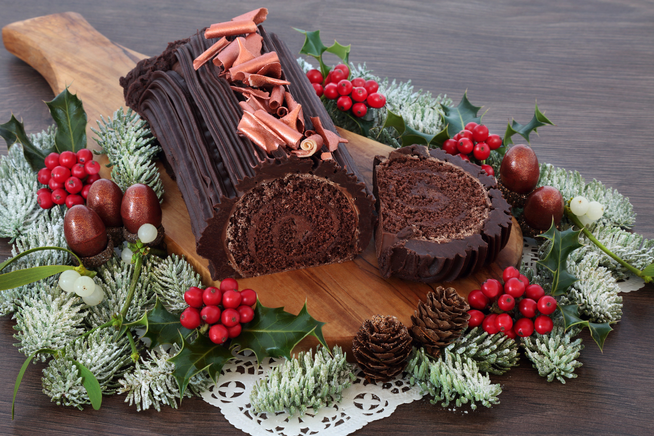 A chocolate yule log sitting on a board with a wreath around it.