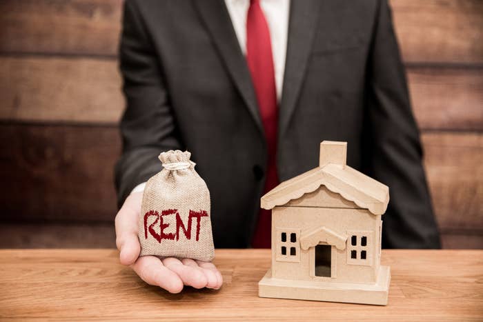 person holding out a small bag labeled &quot;rent&quot; next to a model of a house