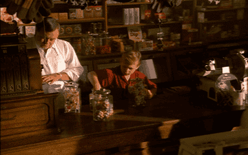 A retro GIF a kid behind a counter taking candy from a candy jar.