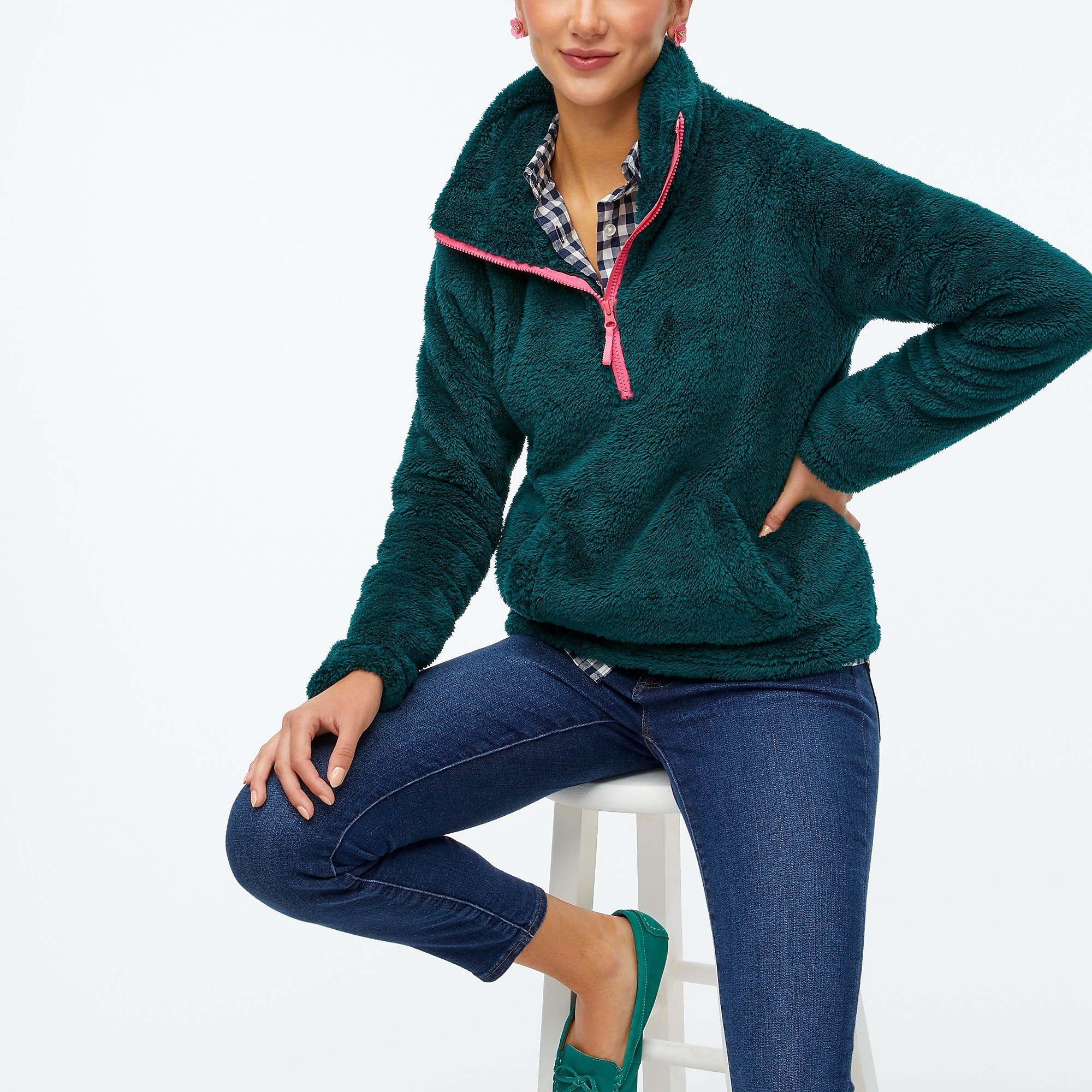 Model wearing a green half zip with jeans and blue and white top