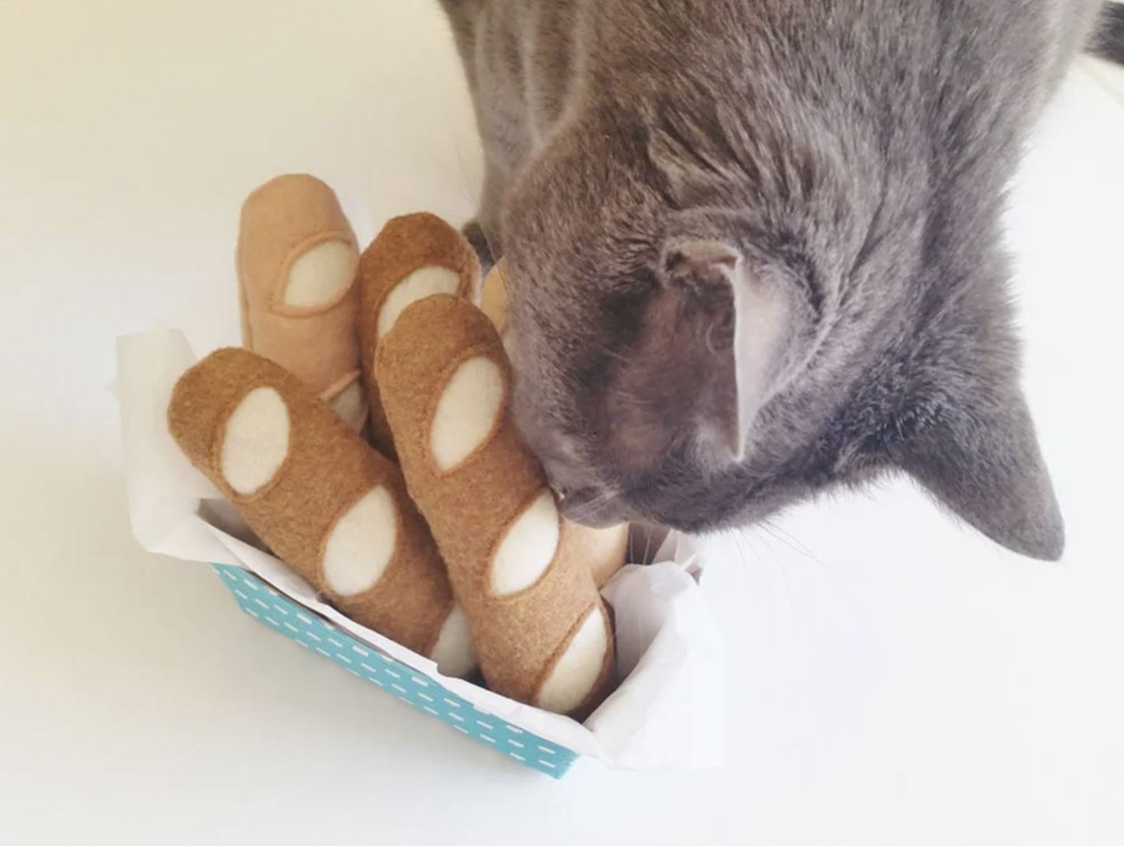 Cat sniffing basket full of bread-shaped plush catnip toys