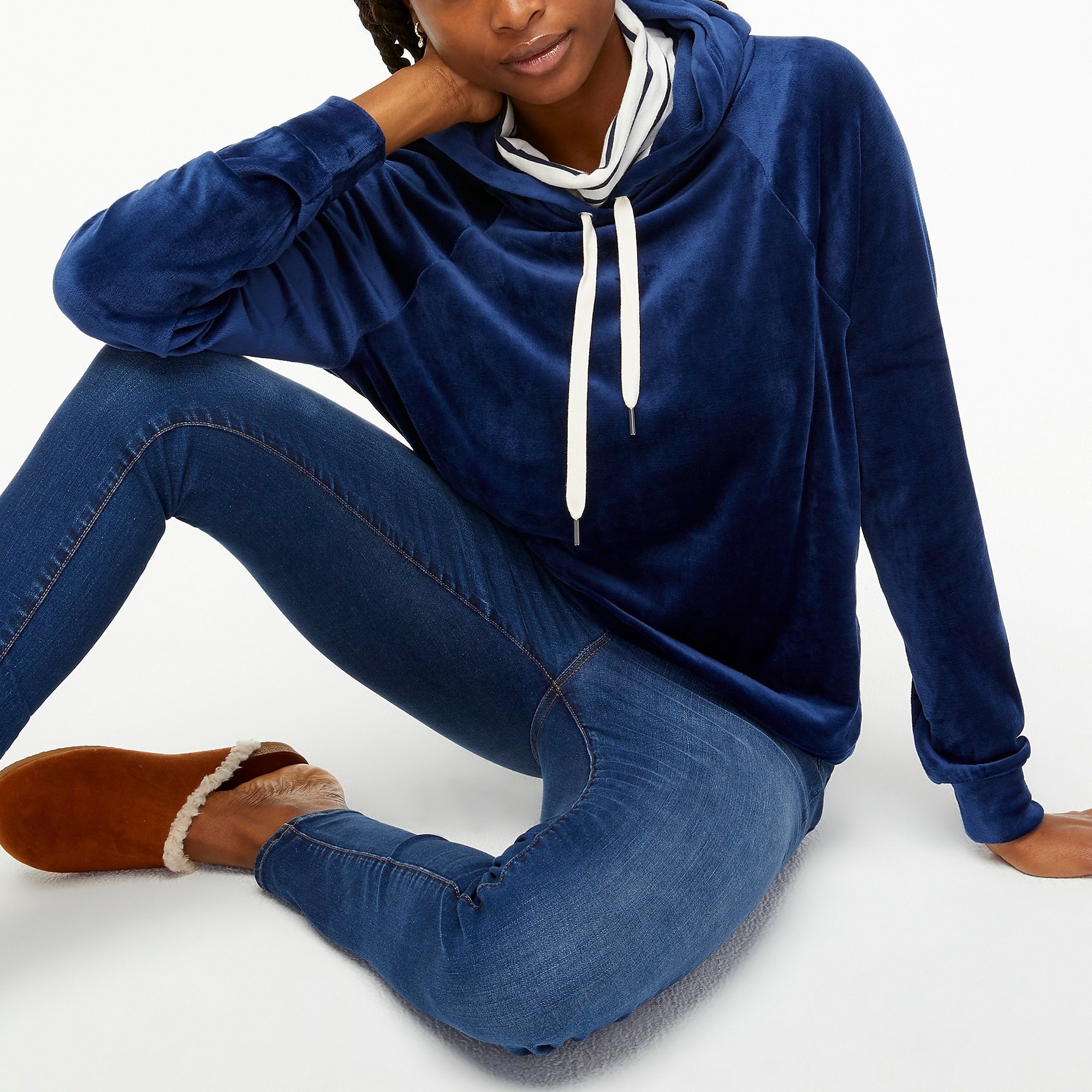Model wearing blue velour sweater with jeans and brown fuzzy slippers