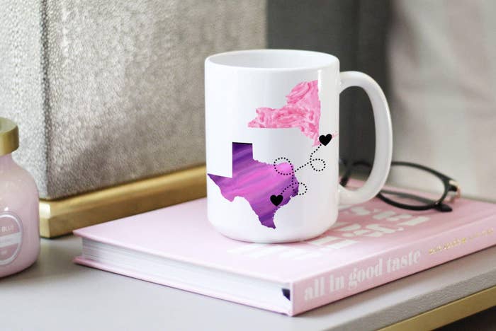 A white mug with two states in different colors with hearts on them and a line connecting the hearts