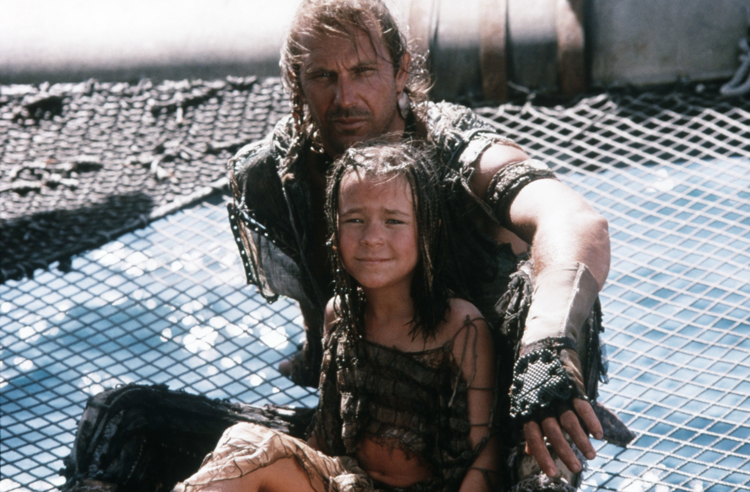 Tina Majorino and Kevin Costner in a post apocalyptic world covered in water, sitting on the net of a ship