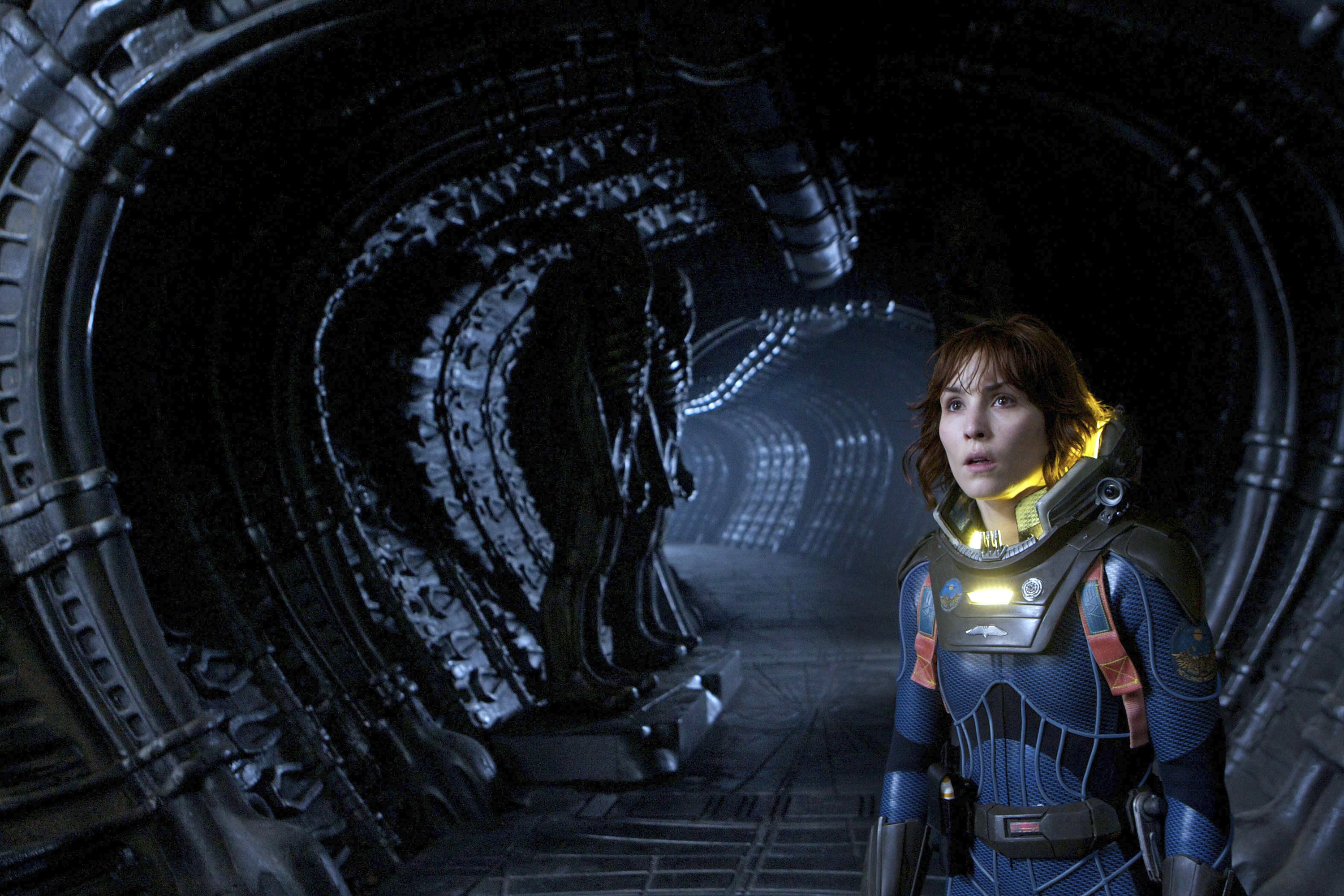 Noomi Rapace in a space suit, walking down the hallway of a dark and creepy alien ship