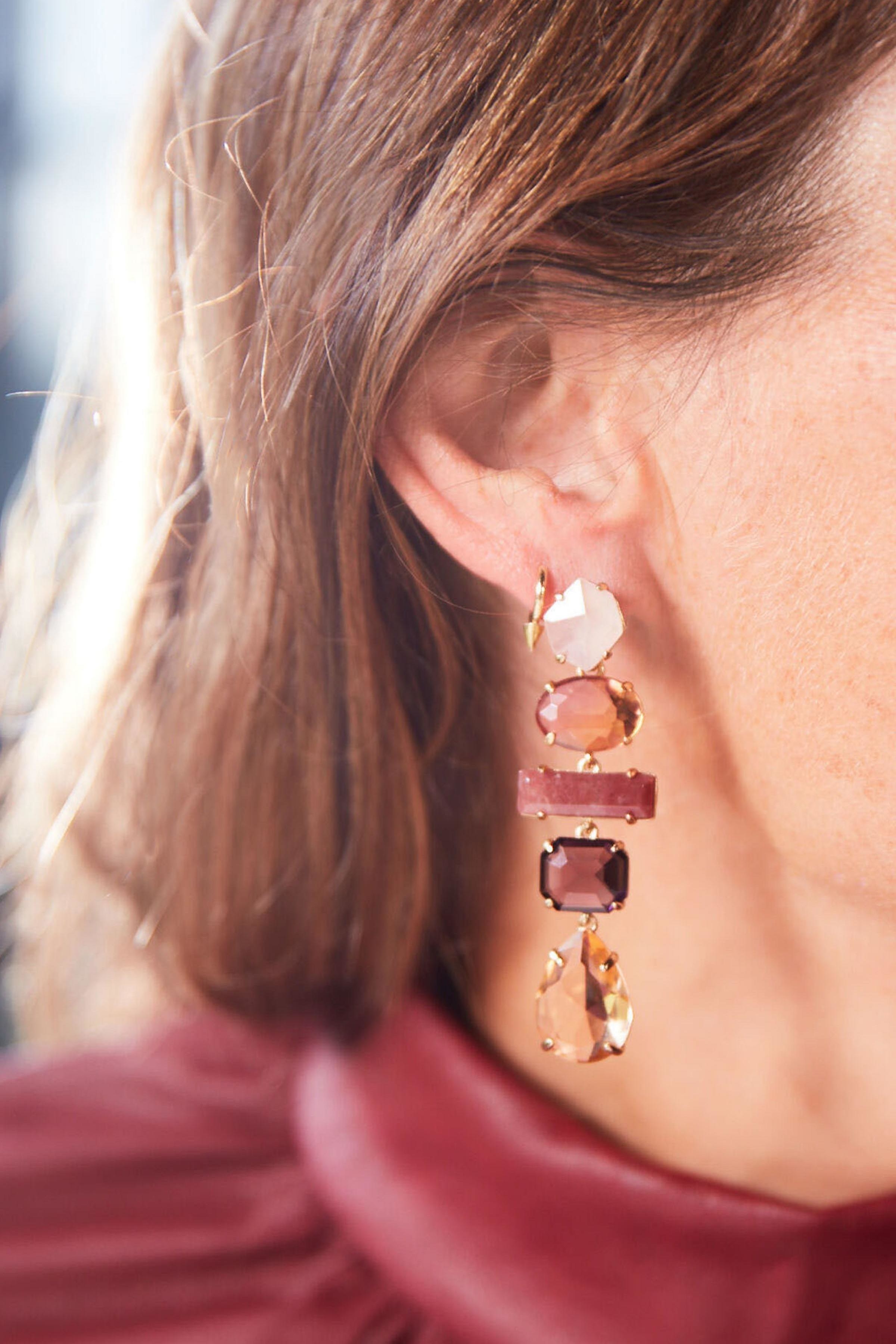 a model wearing a dangling earring with five different stones on it and shades of pink