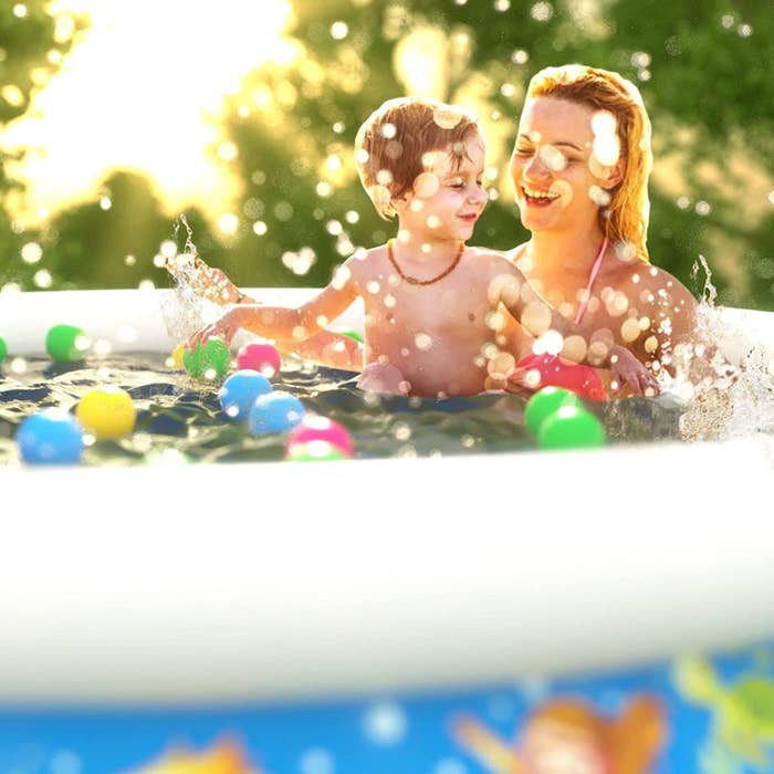 model and small child playing with colorful toys in kiddie pool