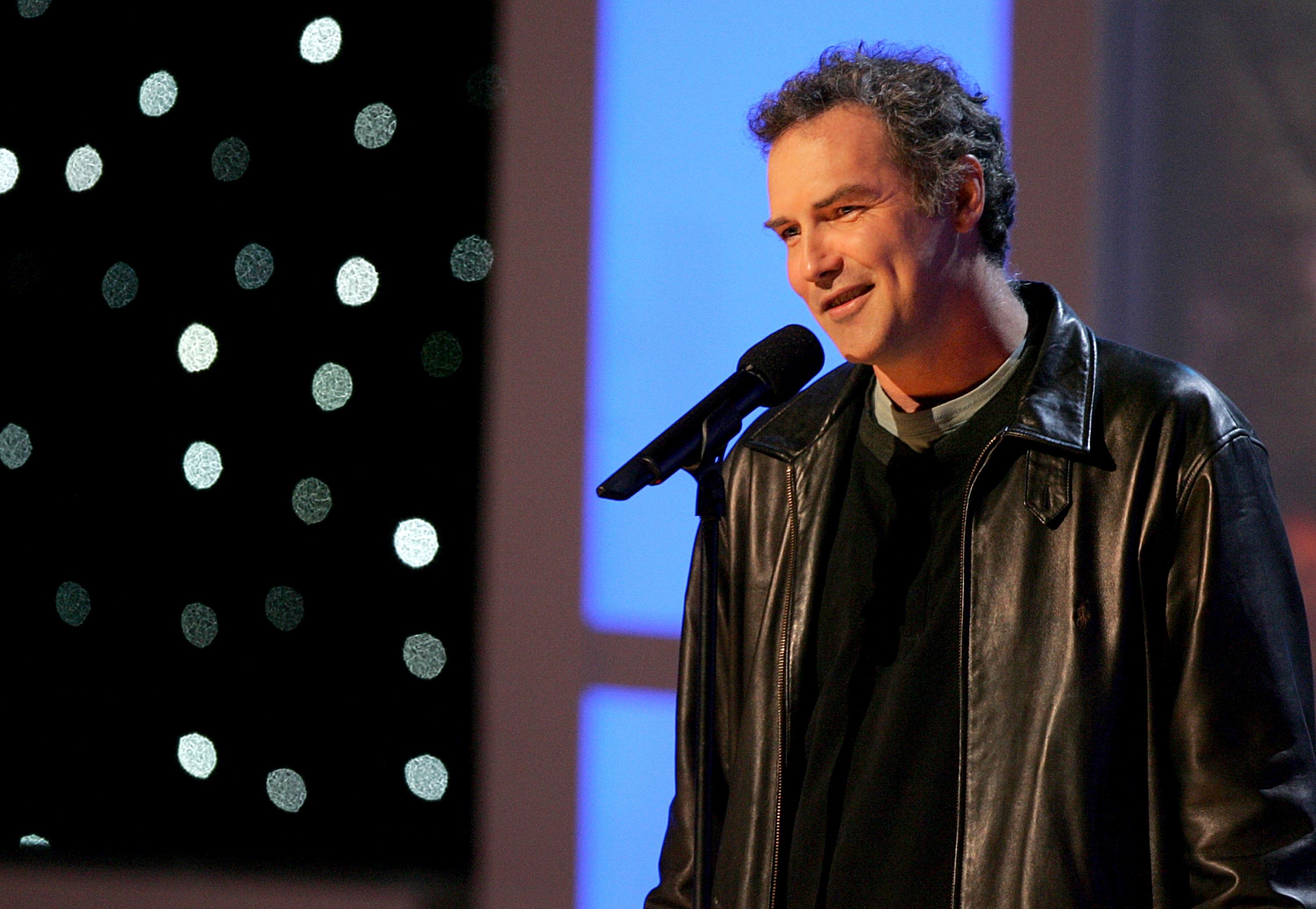 Norm Macdonald at a microphone in a leather jacket