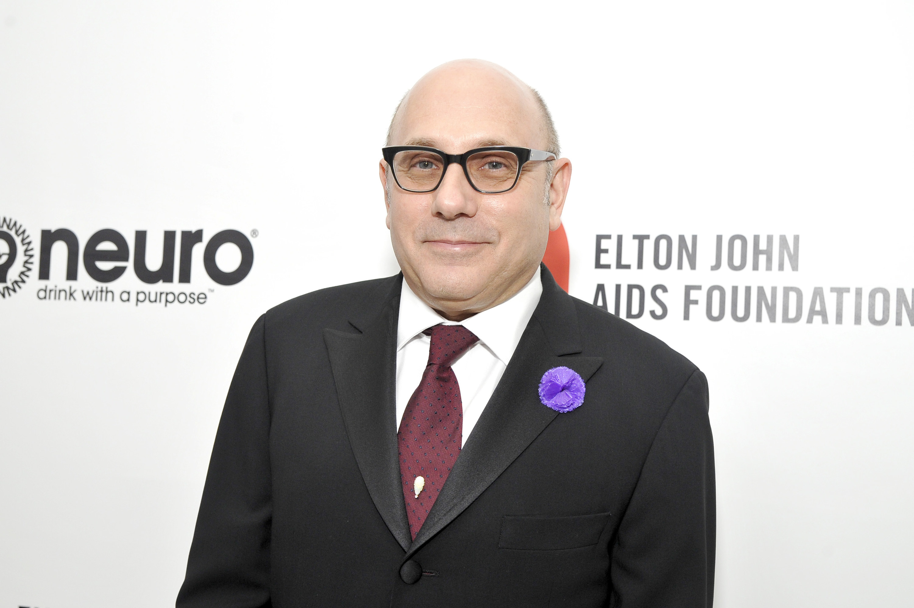 Willie Garson in a suit in front of a wall that reads the Elton John AIDS foundation 