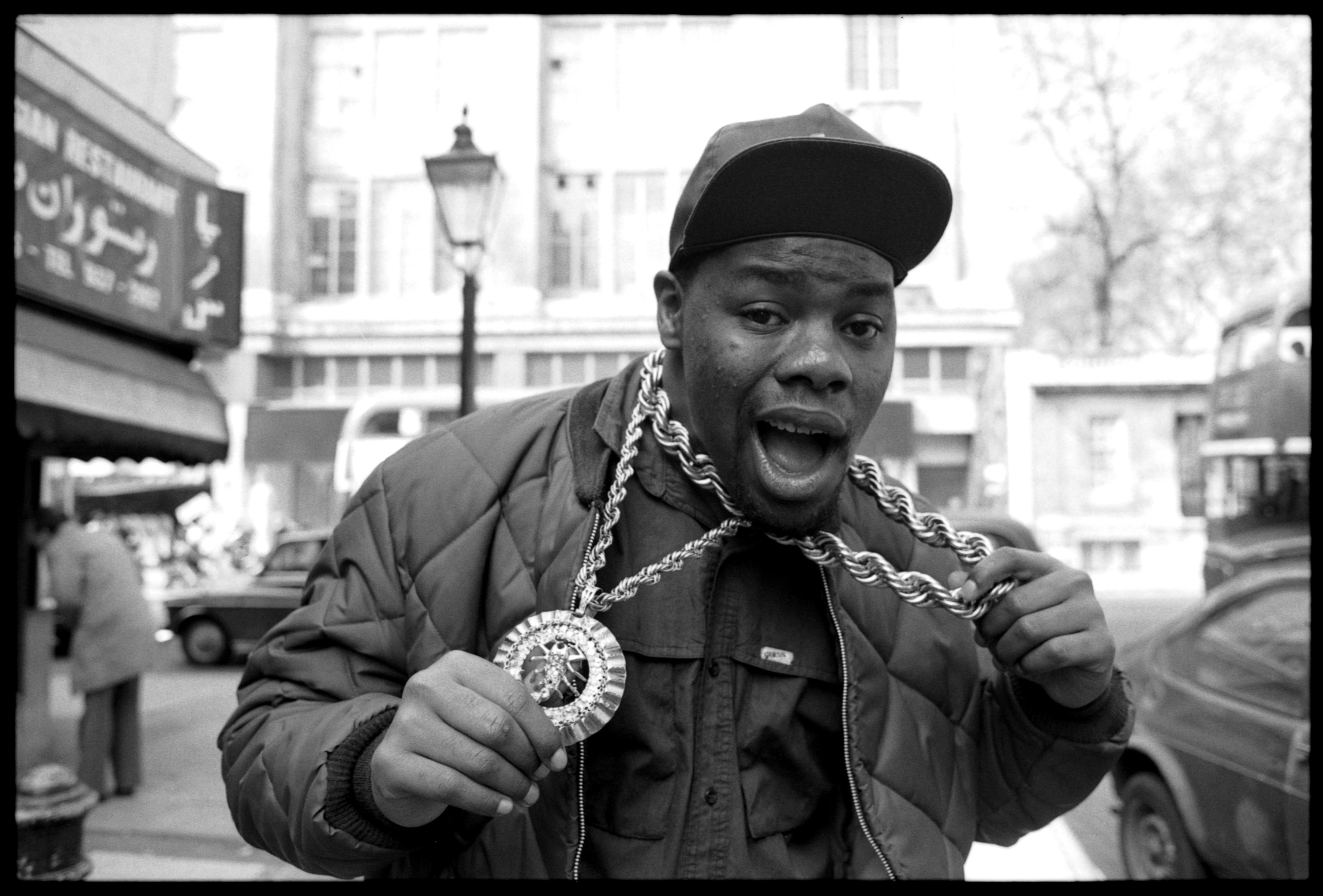 Biz Markie on a street with two chains making a face for the camera