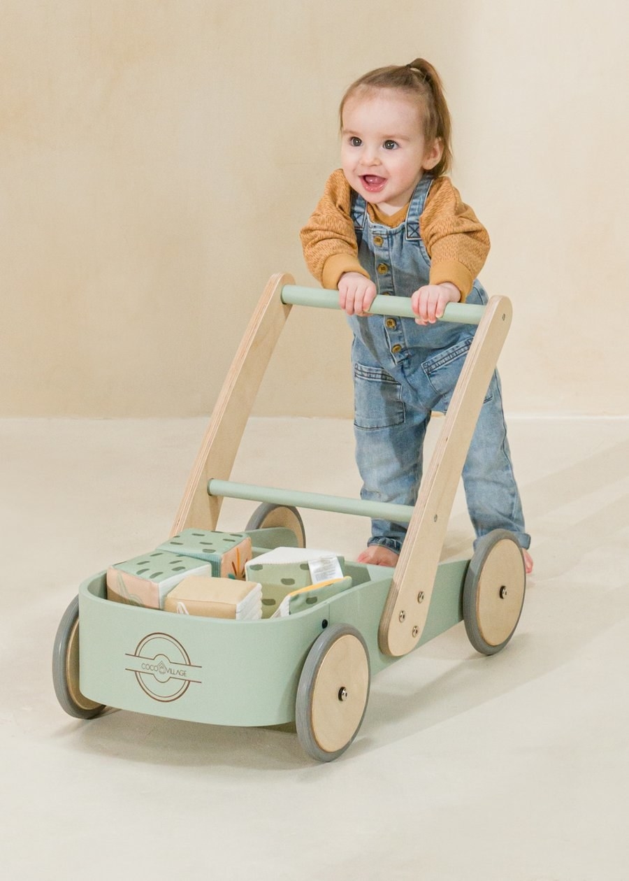a baby pushing a seafrom green wagon with a tall handle