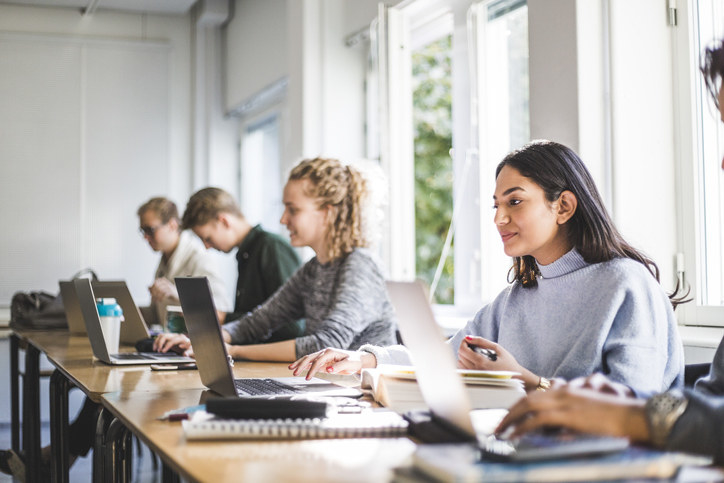 Male and female students using laptops in classroom