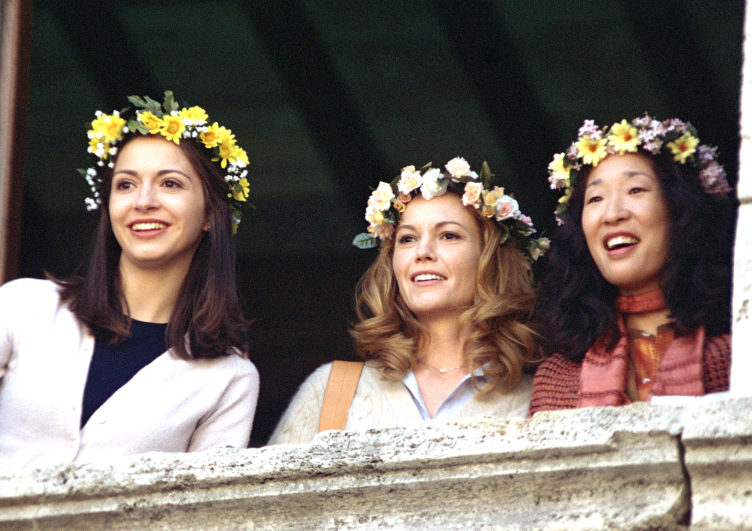 Giulia Steigerwalt, Diane Lane, and Sandra Oh wear flower crowns and look off a balcony