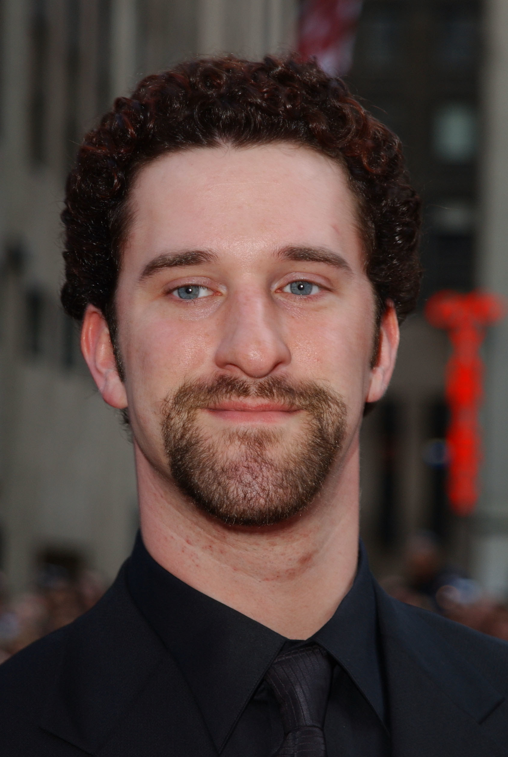 Dustin Diamond in a black suit with a goatee looking past the camera