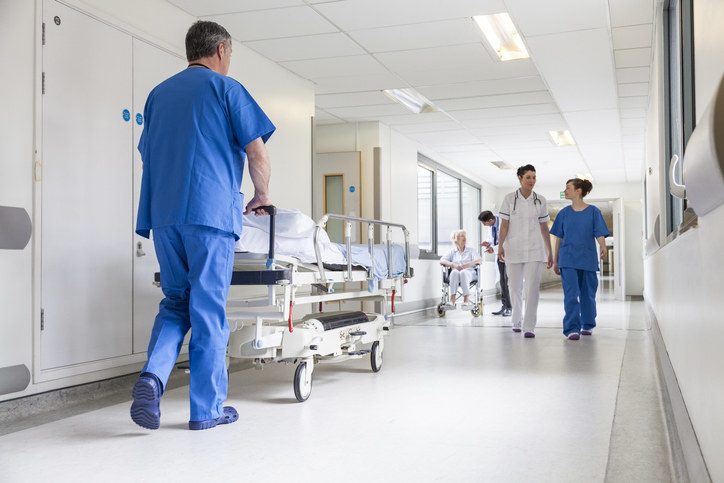 Male nurse pushing stretcher gurney bed in hospital corridor with doctors &amp;amp; senior female patient