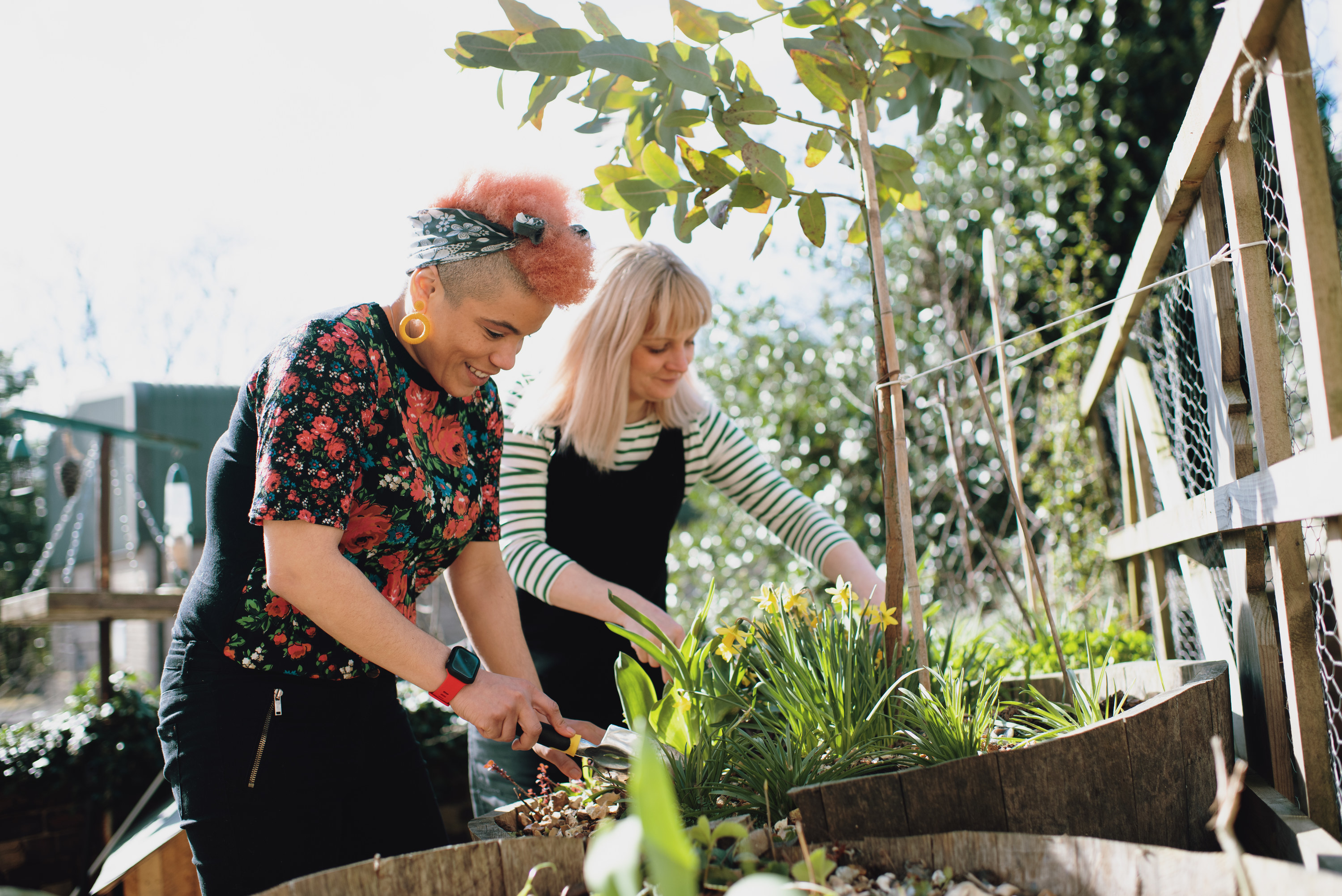 Two stylish people smiling and taking care of plants outdoors.