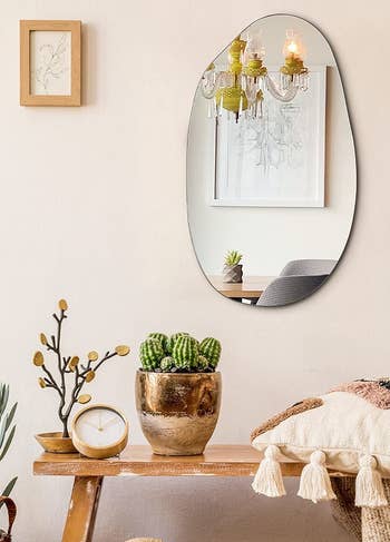 The curvy mirror hanging on a wall above a bench, plants, and pillows
