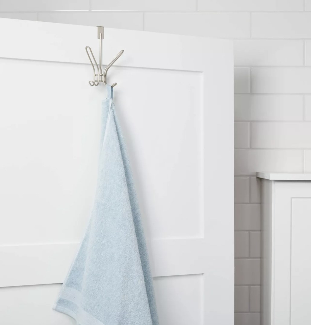 A silver/satin colors hook is over a white door and holding a powder blue towel