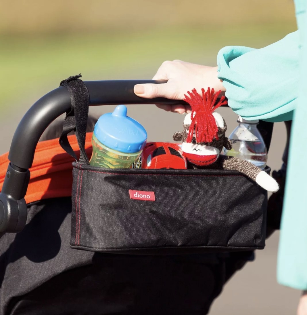 The black organizer has a red tag that says &quot;diono&quot; is holding drinks, a sock monkey and toy car and is attached to a black stroller handle