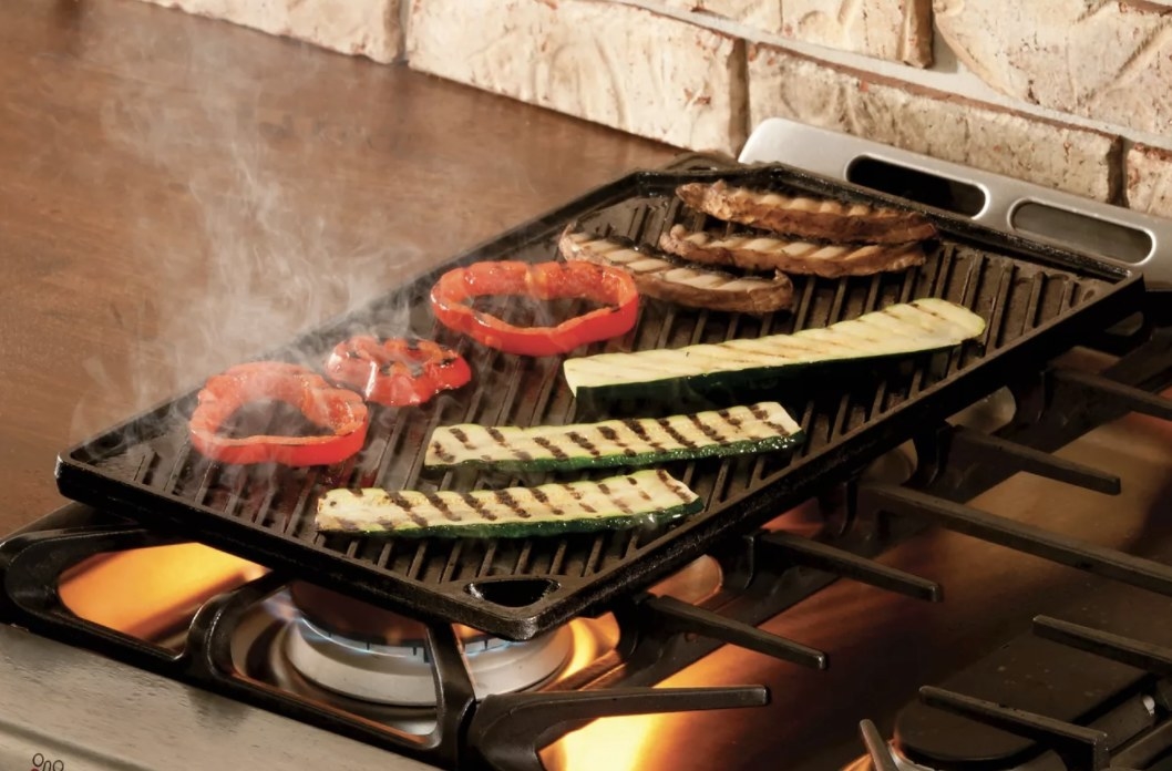 The black griddle has raised panels that are searing the vegetables on top of a gas stove