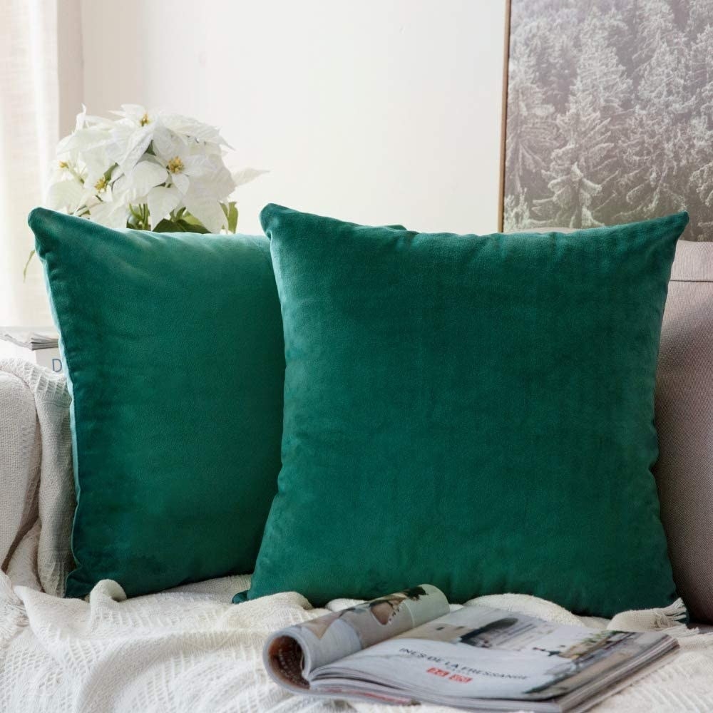 two velvet pillow covers in dark green sitting on a gray couch.