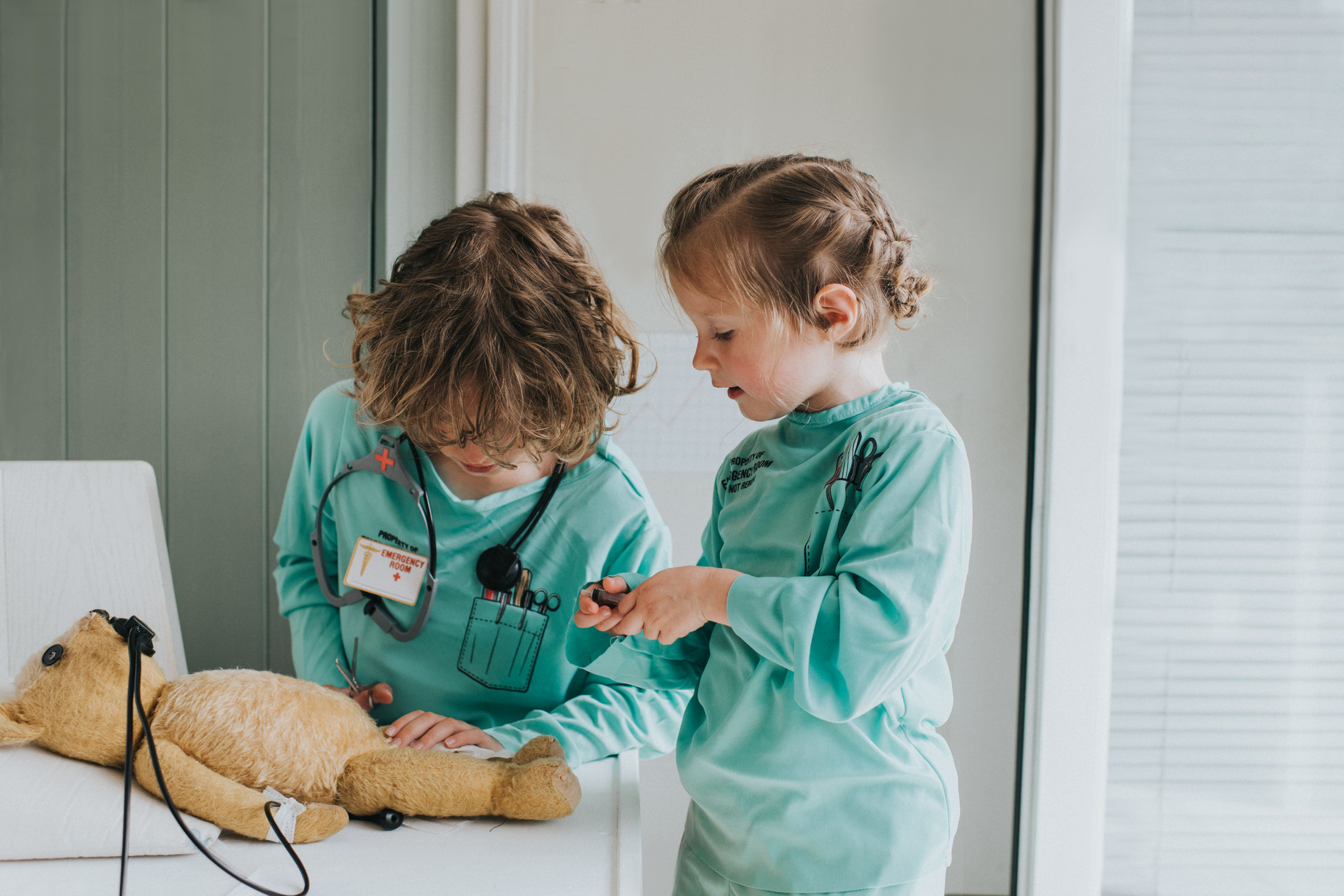 Two children play doctor with a teddy bear