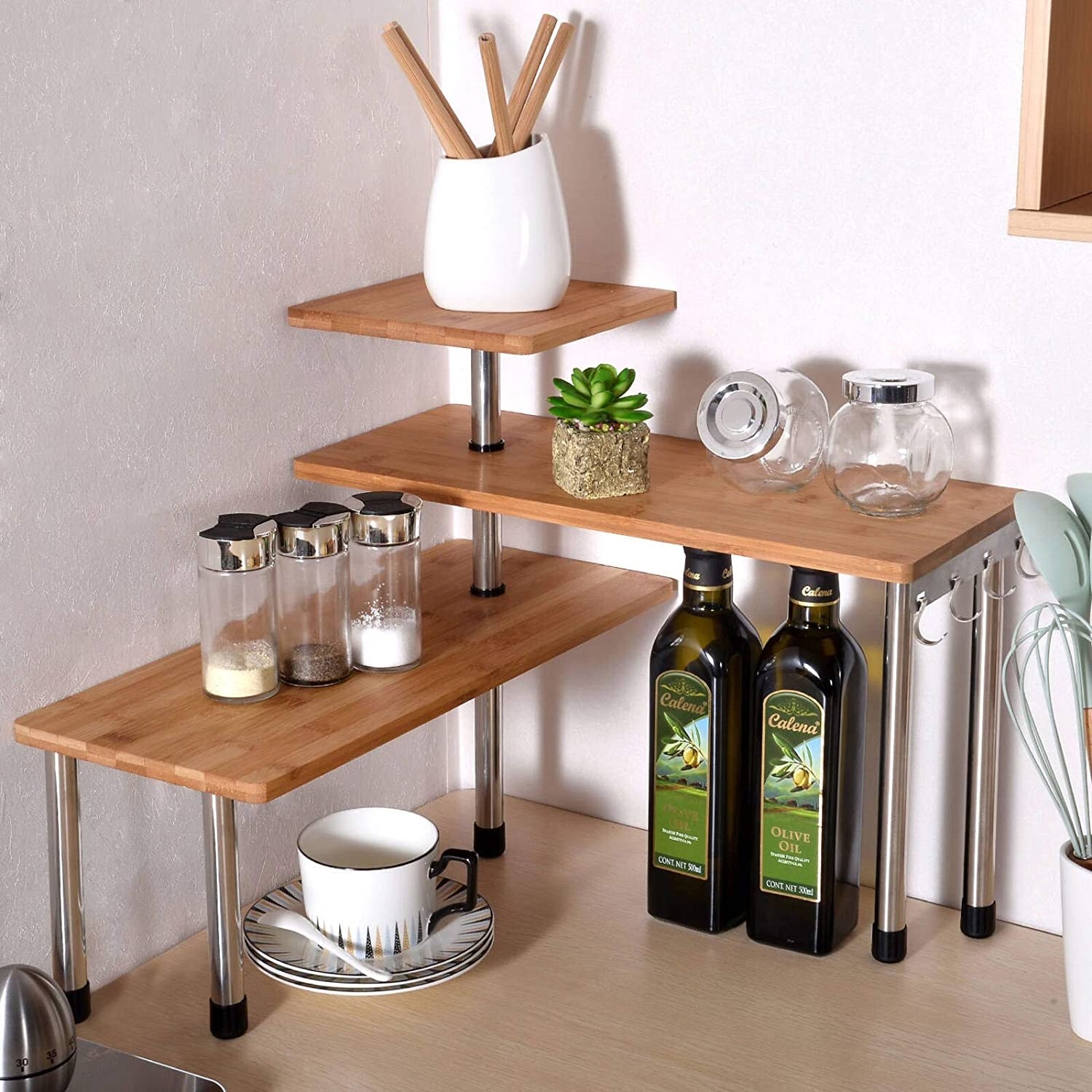 3-tier organization shelf arranged in the corner on a kitchen counter with spices, olive oil, and dishes resting on it