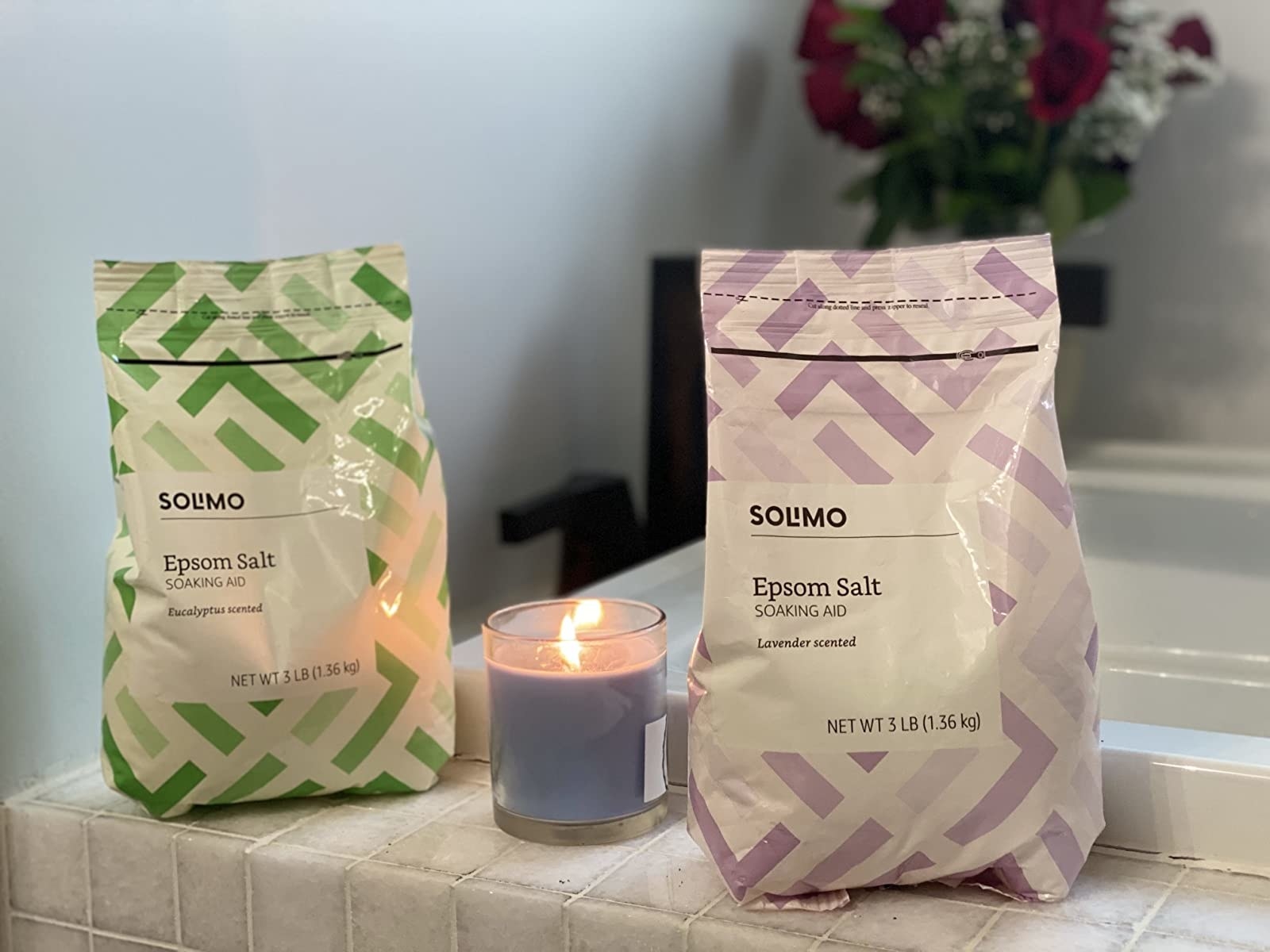 two bags of the epsom salt next to a candle on a bathtub edge