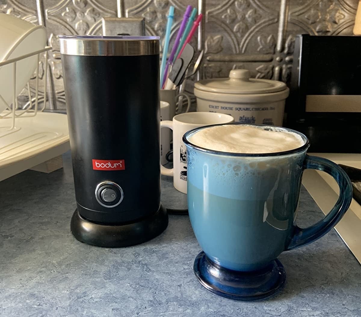 the electric milk frother with a cup next to it with frothed foam on top