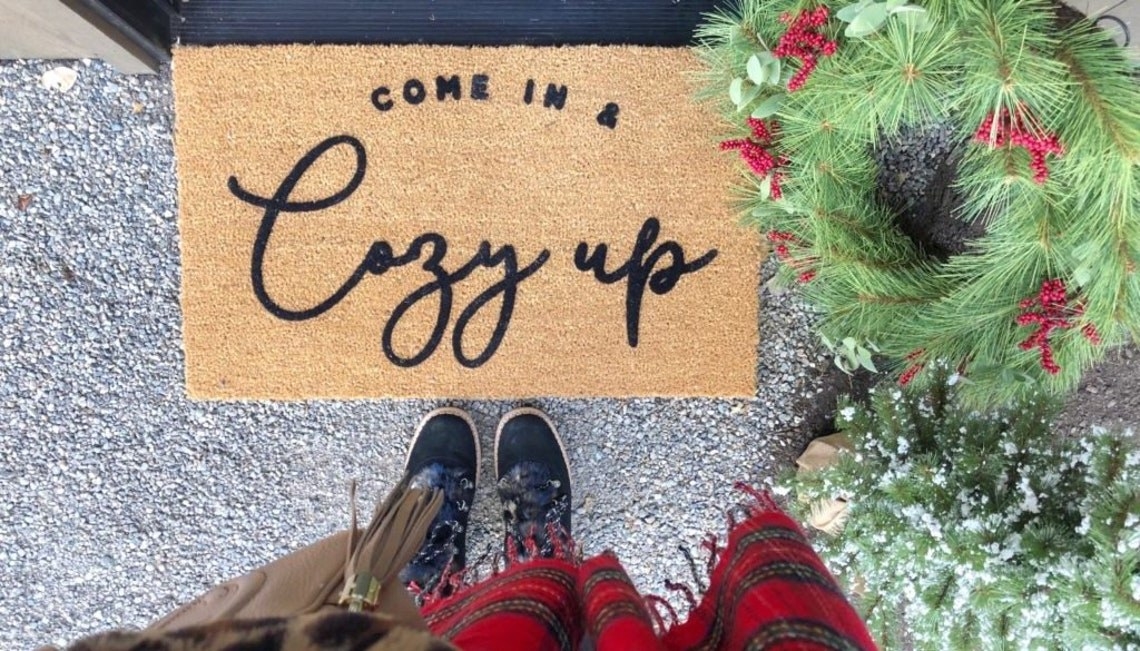 person standing above door mat that reads &quot;Come in &amp;amp; cozy up&quot;