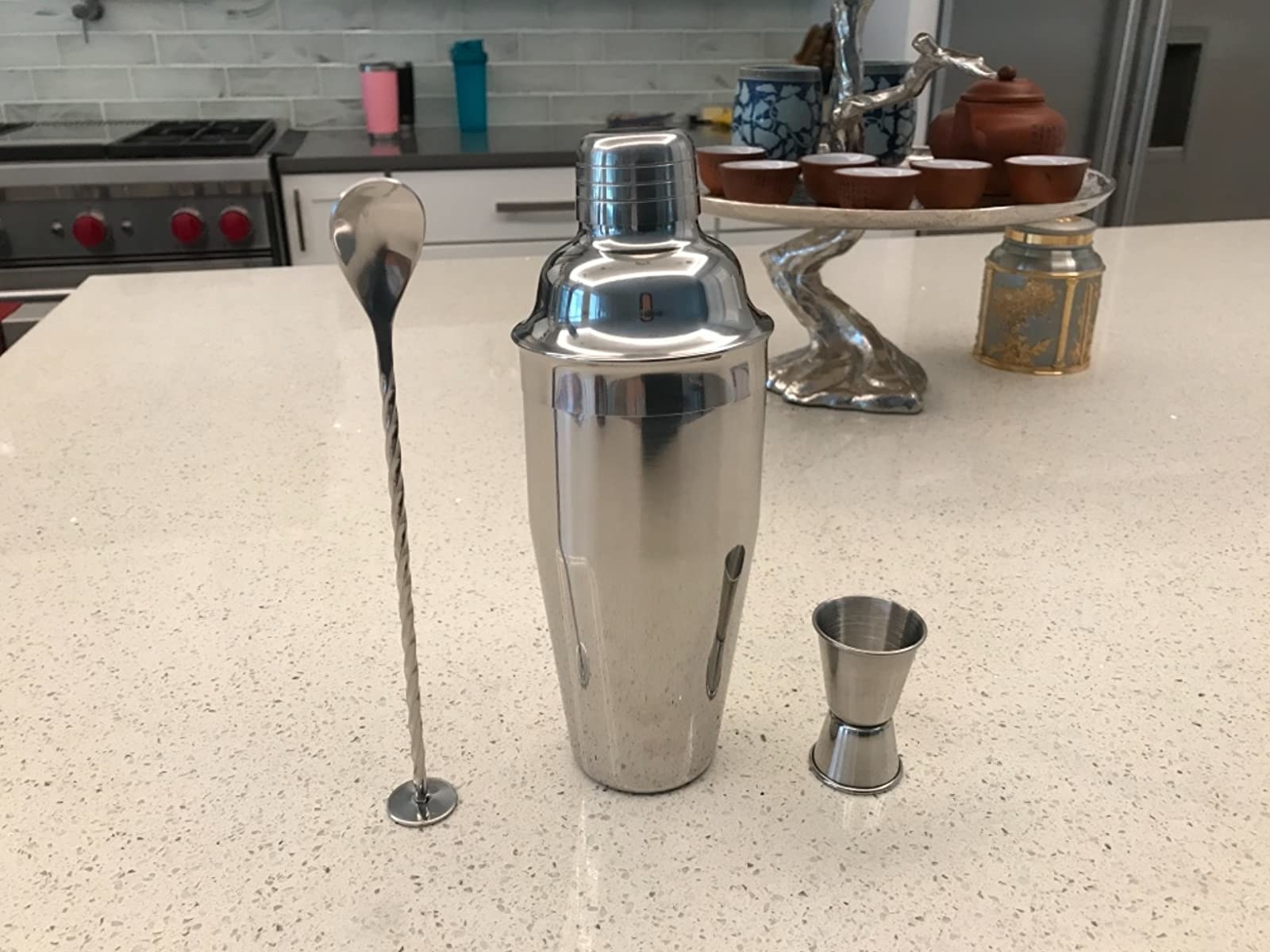 the silver cocktail shaker with lid, spoon, and measuring cup