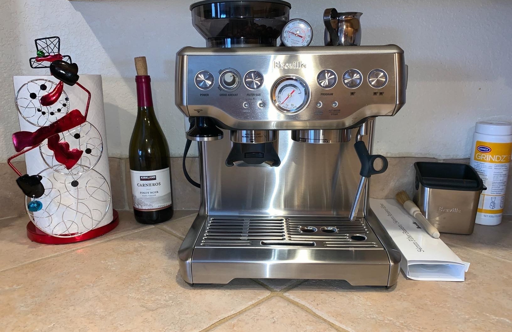 the silver espresso machine on a counter next to a snowman and a bottle of wine