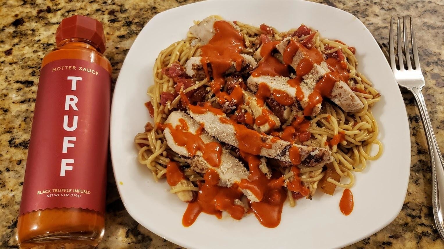 reviewer image of the truffle hot sauce bottle next to a plate of food drizzled in the hot sauce