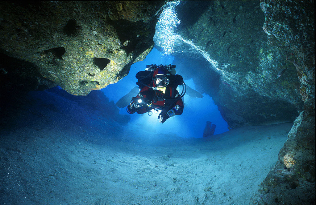 a scuba diver swimming into a dark narrow cave
