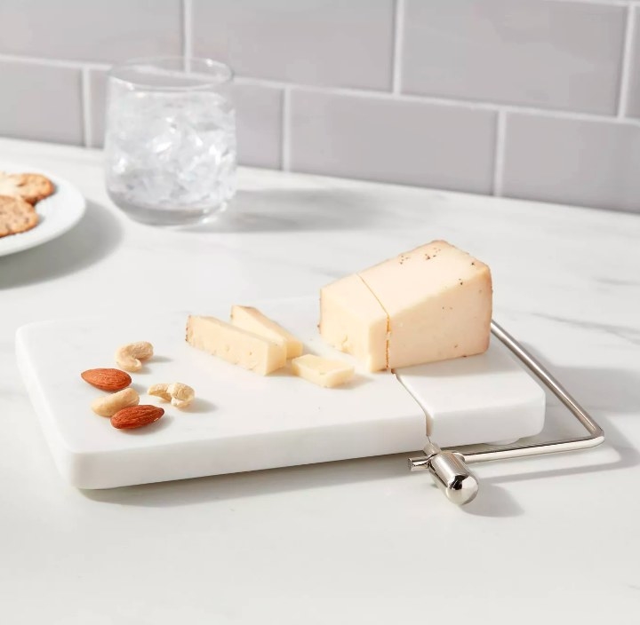 The white marble slicer with a partially sliced block of parmesan cheese and nuts on the serving board