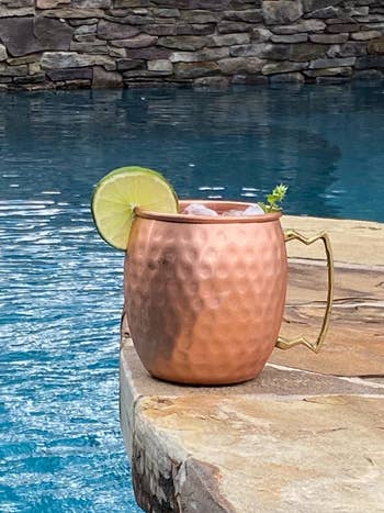 reviewer image of the gold copper mug sitting by a pool