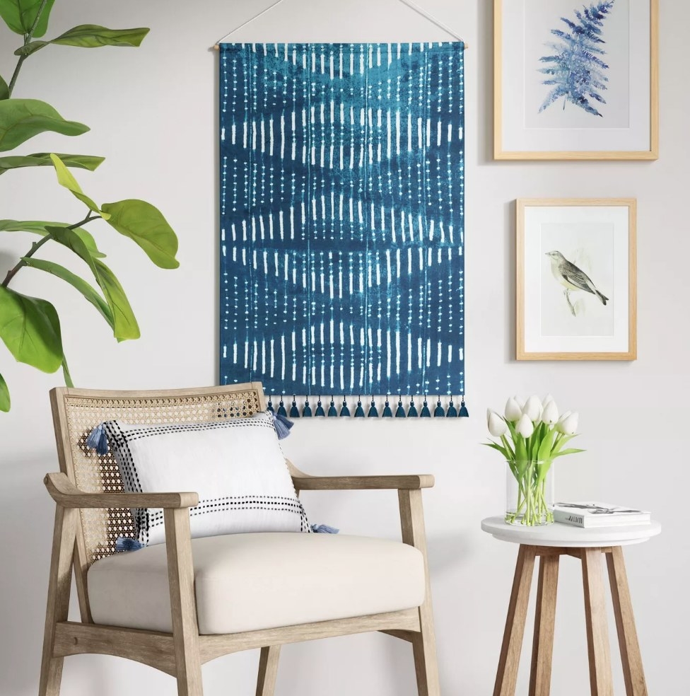 Blue tassel tapestry hanging on wall behind chair and table