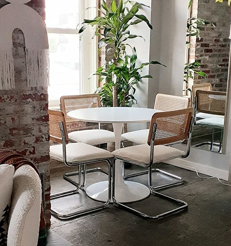 Reviewer shows four of the chairs with white cushions sitting under their round dining table.