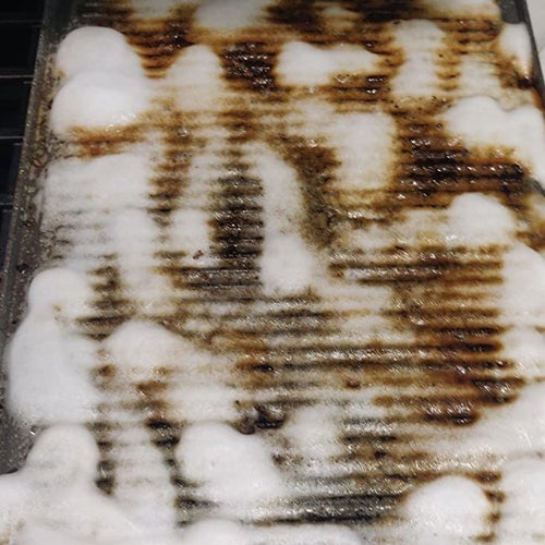 the dirty baking sheet with white cleaning foam on it