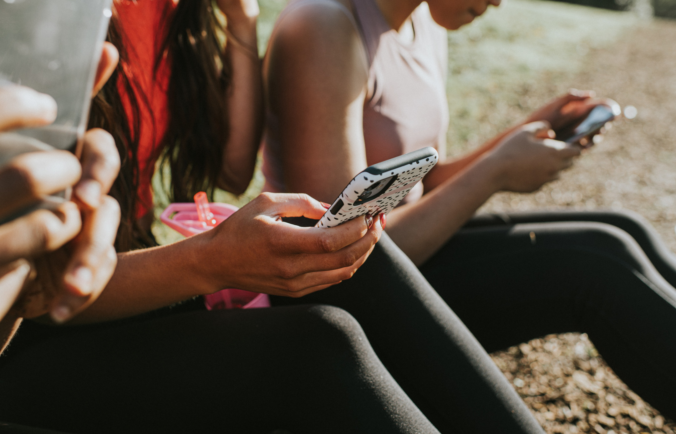 Teens sit outside scrolling on their phones