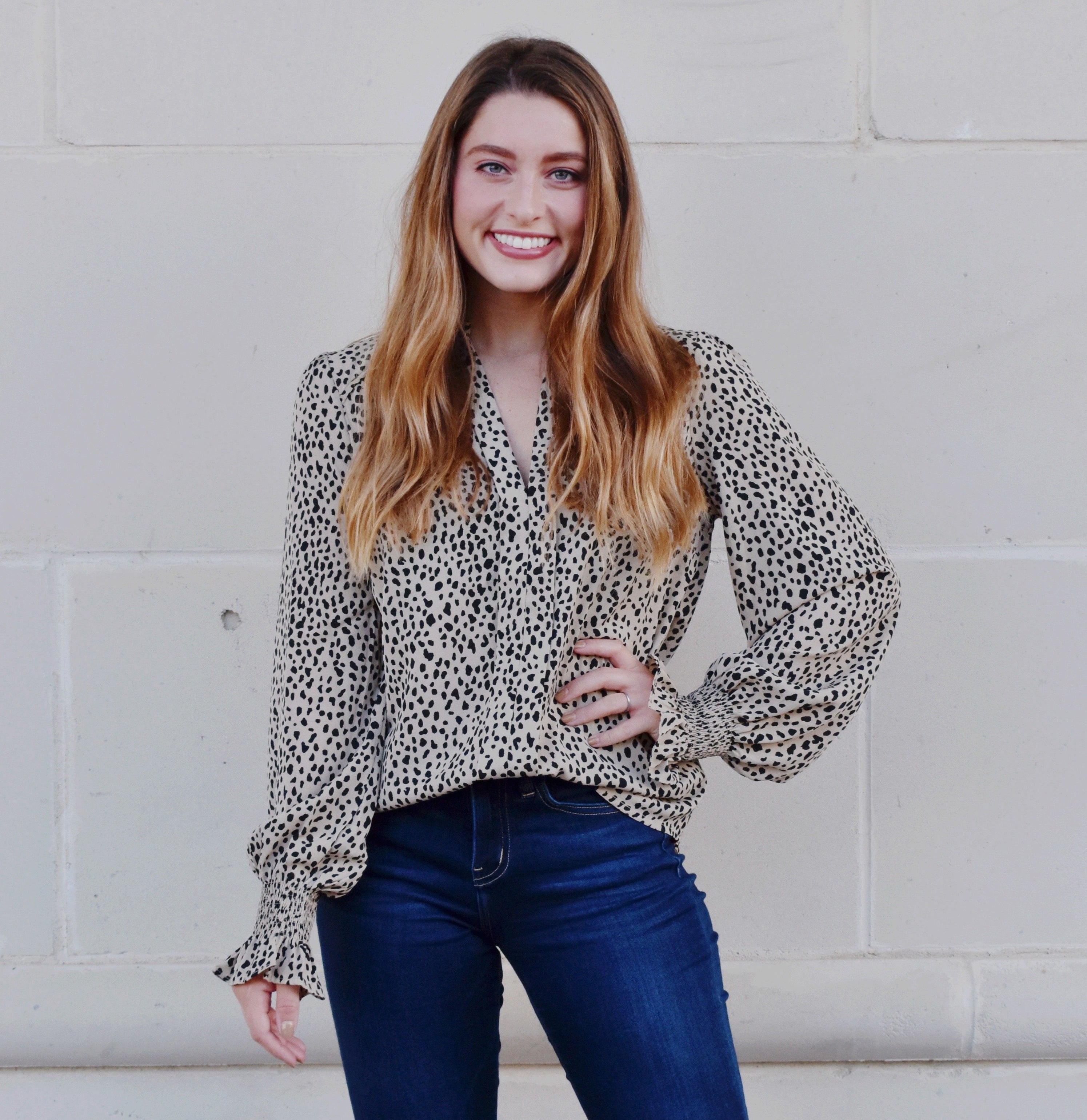 Model is wearing a taupe blouse with black irregular dots all throughout and balloon sleeves