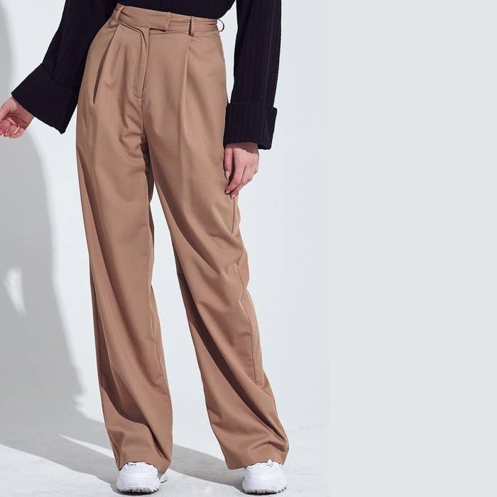 Model is wearing light brown loose trousers and white tennis shoes