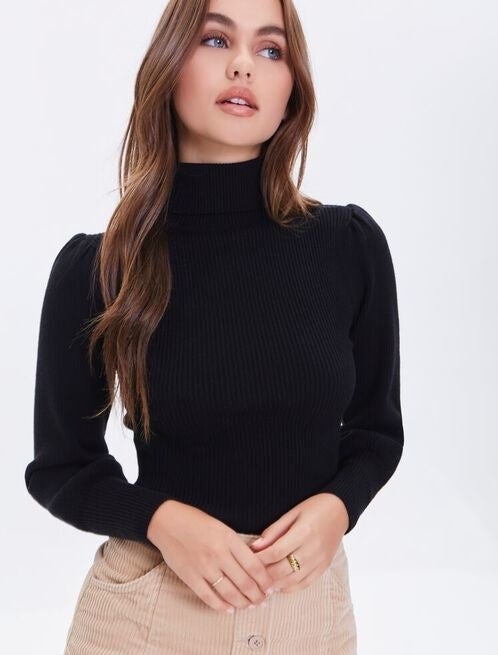 Model is wearing a black turtleneck sweater and a beige skirt