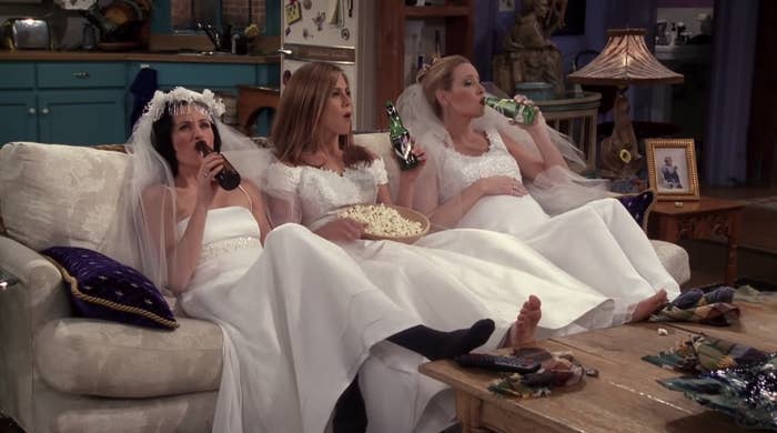 The women of Friends sitting on a couch in wedding dresses, all drinking from bottles