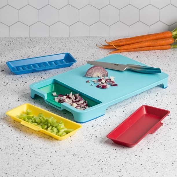 the cutting board with an onion being cut and chopped celery in one of the removable compartment trays
