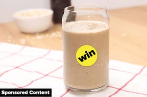 A glass of the smoothie on a white towel with oats in the background. A "WIN" sticker is on top of the glass.